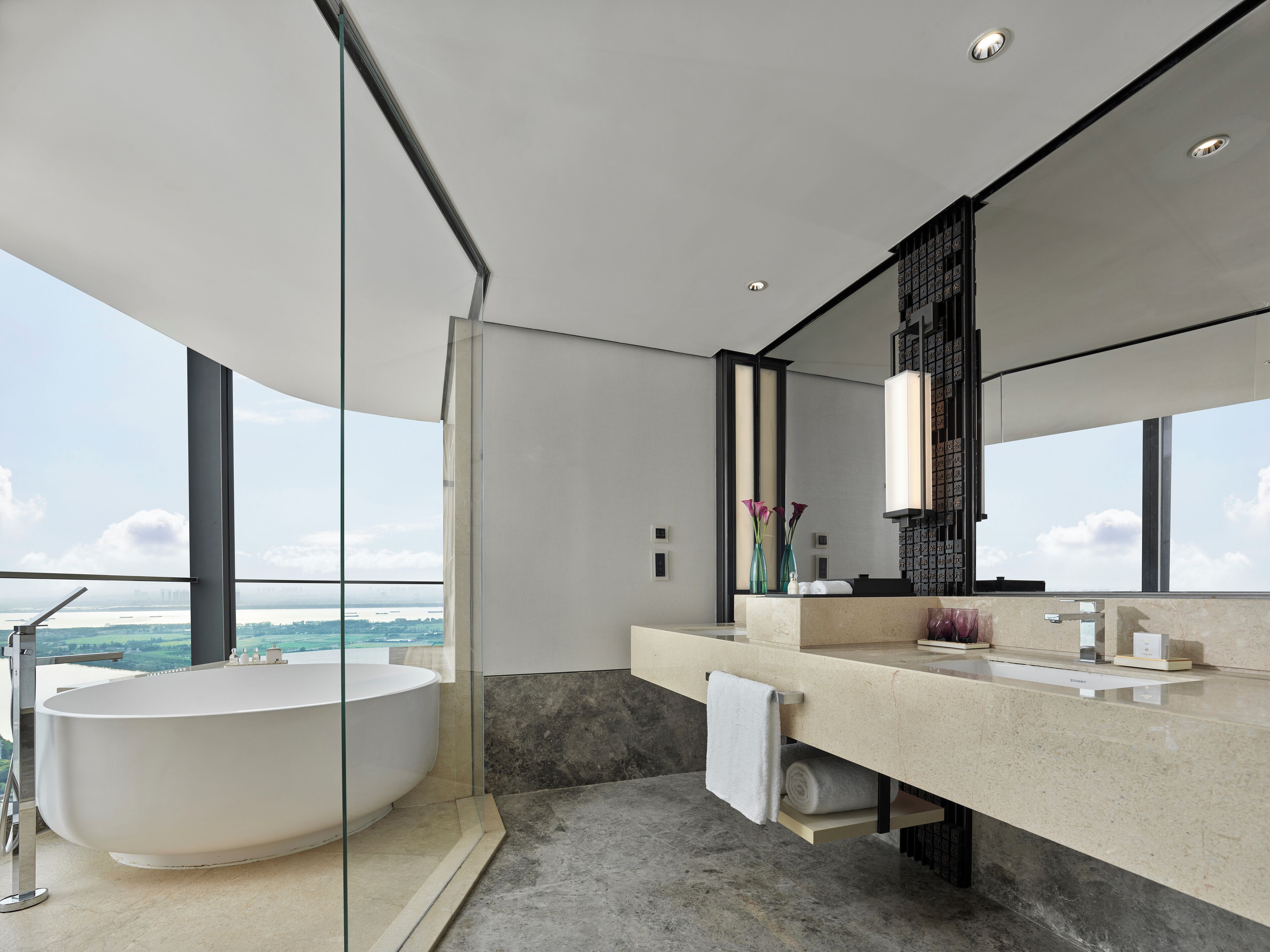A modern bathroom with a freestanding bathtub, a large mirror, and a view of the city.