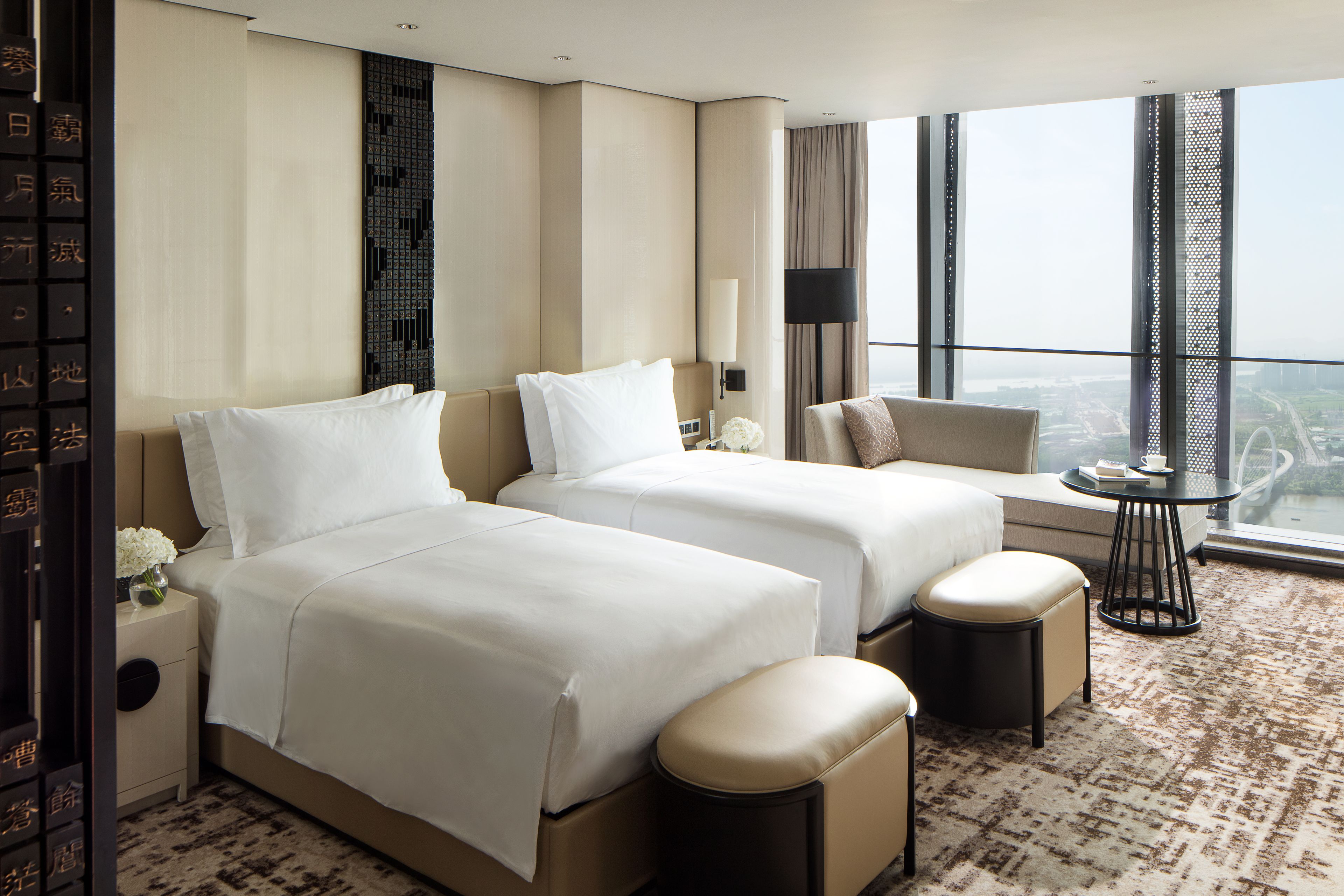 A hotel room with two beds, a sofa, a small table, and a view of the city.