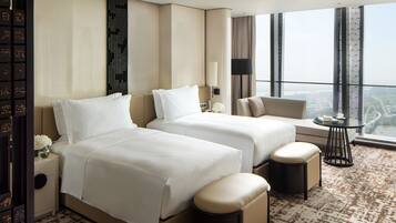 A hotel room with two beds, a sofa, a small table, and a view of the city.