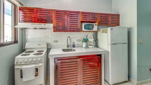 A compact kitchen with a stove, microwave, and refrigerator, wooden cabinets, and a window.
