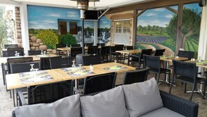 A restaurant with outdoor seating, tables with menus, and a mural of a landscape.