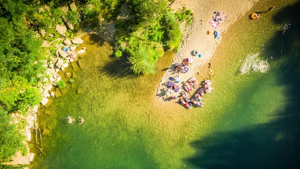 An aerial view of a beach with clear water, surrounded by greenery and rocks.