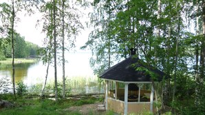 A small gazebo with a black roof and white walls, surrounded by trees and a body of water. - Raikala (Savonlinna)