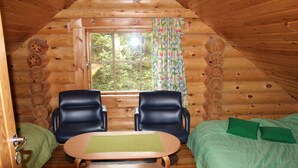 A cozy cabin room with a wooden interior, a small table, two chairs, a bed with green bedding, and a window with a floral curtain. - Raikala (Savonlinna)