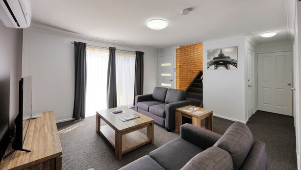 A modern living room with a sofa, a coffee table, a TV, and a staircase leading to another room.