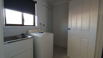 A compact kitchen with a built-in sink, a washing machine, and a door leading to another room.