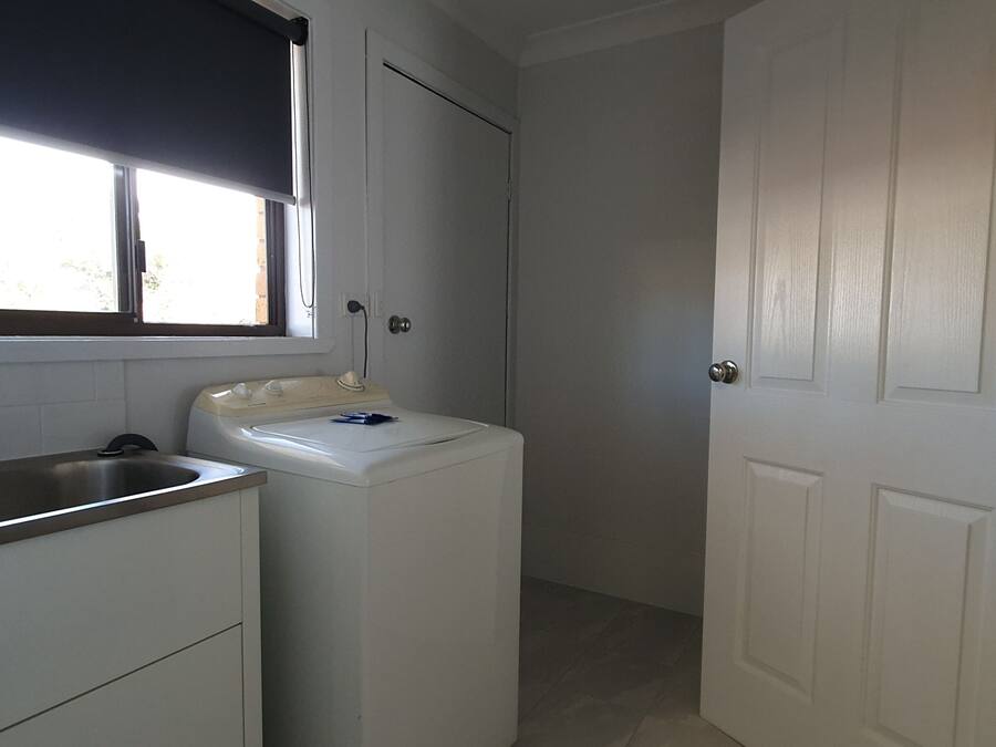 A compact kitchen with a built-in sink, a washing machine, and a door leading to another room.