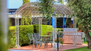 A gazebo with a metal roof, surrounded by well-maintained hedges and a barbecue area.