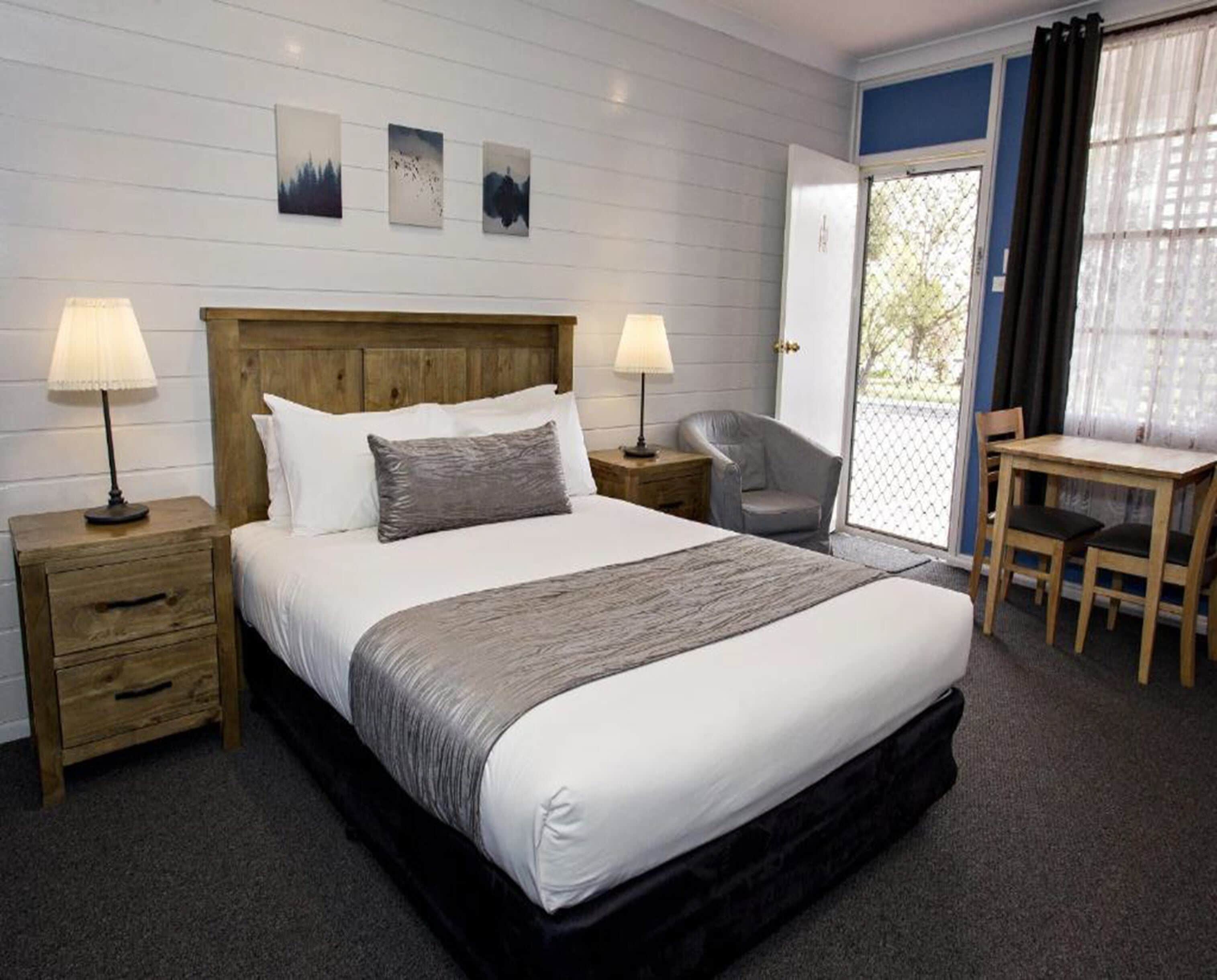 A hotel room with a bed, two bedside tables, a chair, a desk, and a view of the outdoors.