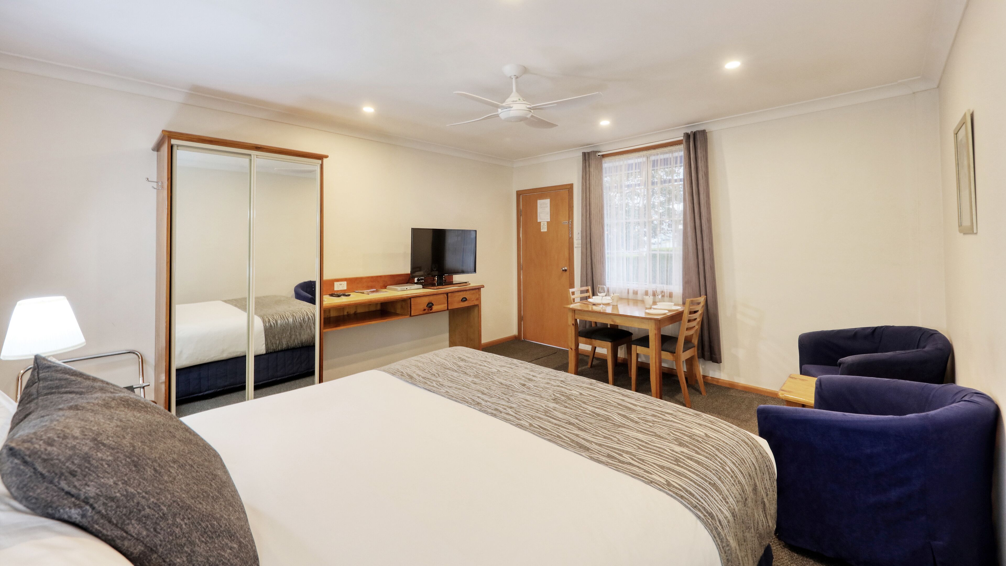 A hotel room with a bed, a desk, a chair, a TV, and a dining table with chairs.
