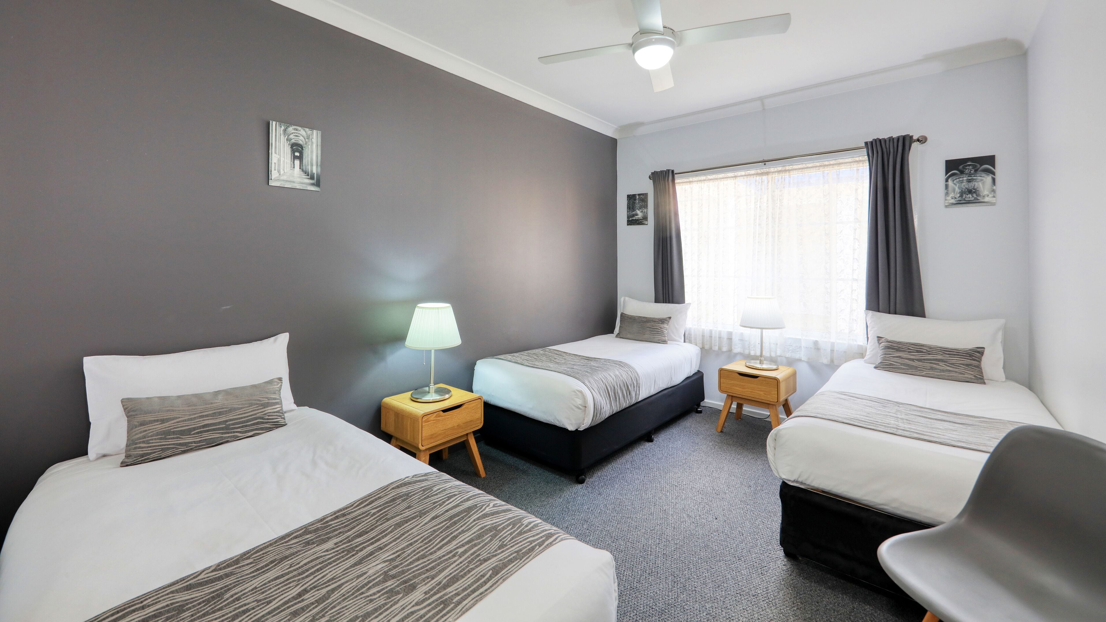 A hotel room with two beds, a ceiling fan, and a window with curtains.