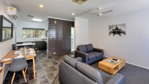 A modern living room with a grey sofa, a wooden coffee table, and a dining area with a table set for four.