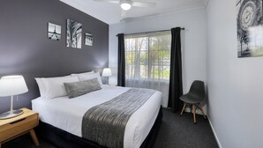 A hotel room with a bed, a nightstand, a chair, and a window with curtains.