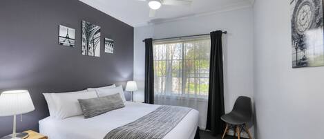 Una habitación de hotel con una cama, una mesita de noche, una silla y una ventana con cortinas.