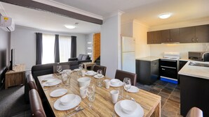 A modern dining area with a wooden table set for a meal, a kitchen with dark cabinets and stainless steel appliances, and a living area with a sofa and a TV.