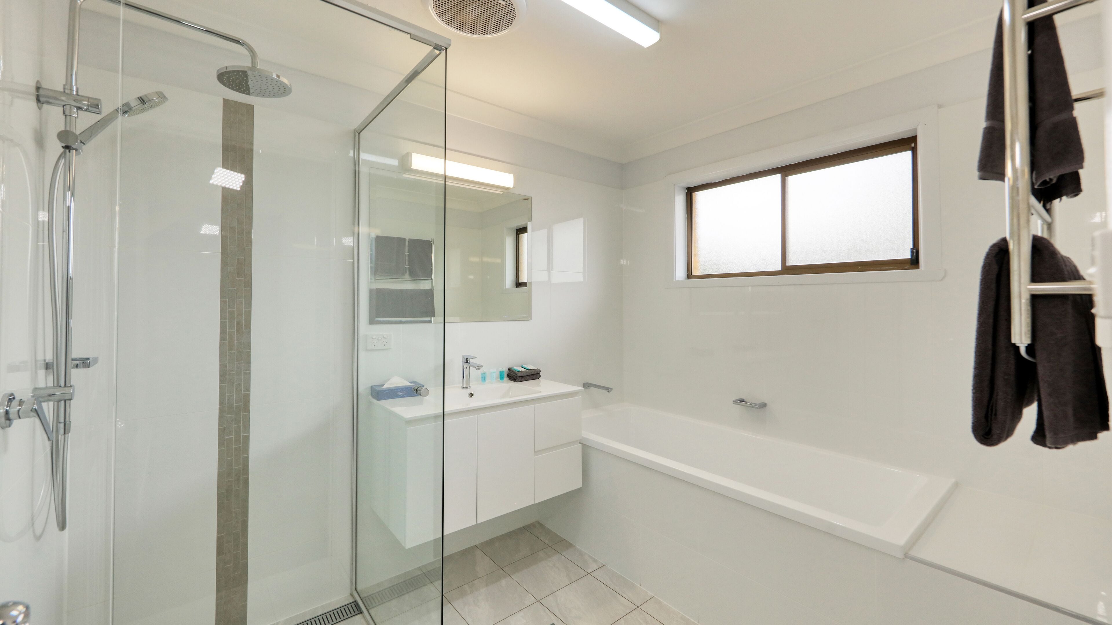 Un baño moderno con ducha de vidrio, lavamanos blanco con espejo y una bañera grande.