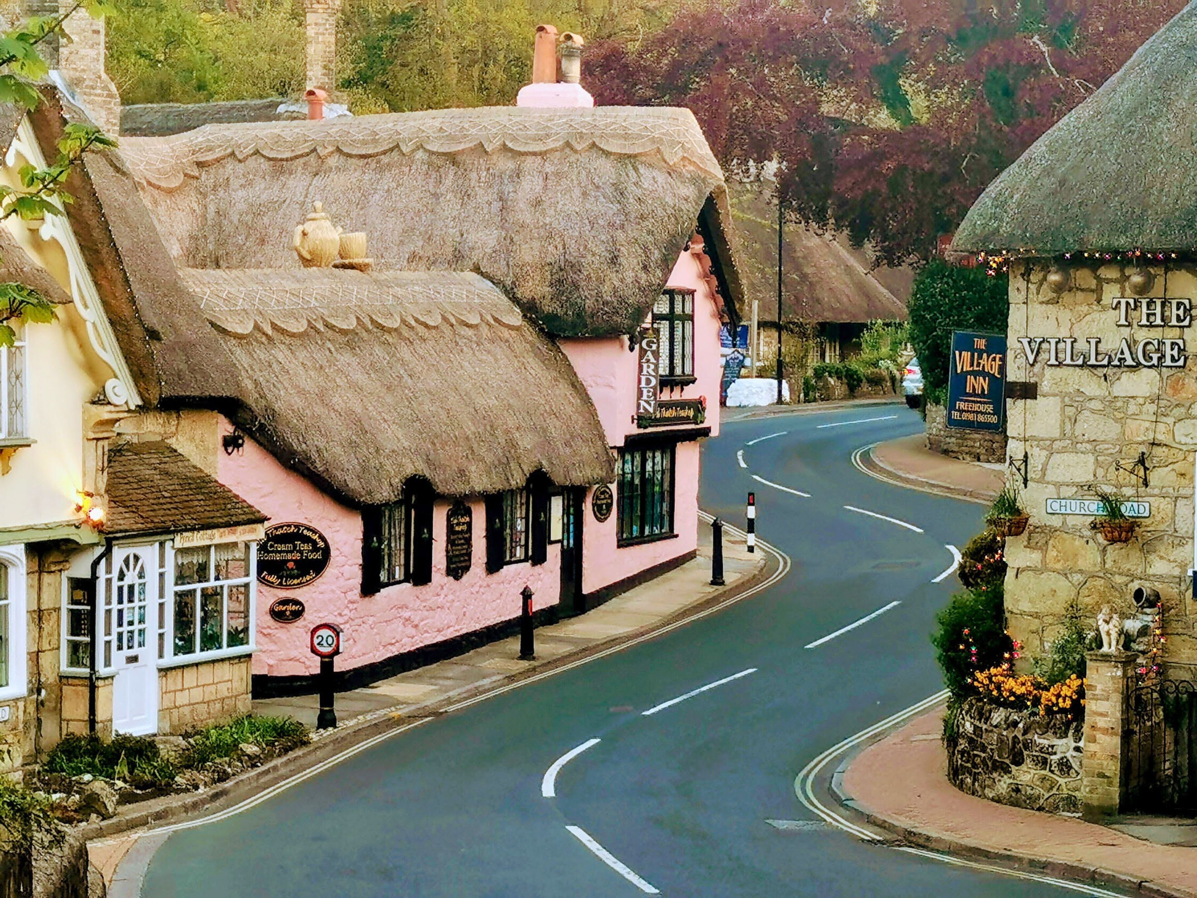 Un edificio rosa con techo de paja, un letrero que dice 'The Village Inn' y una señal de límite de velocidad de '20'.