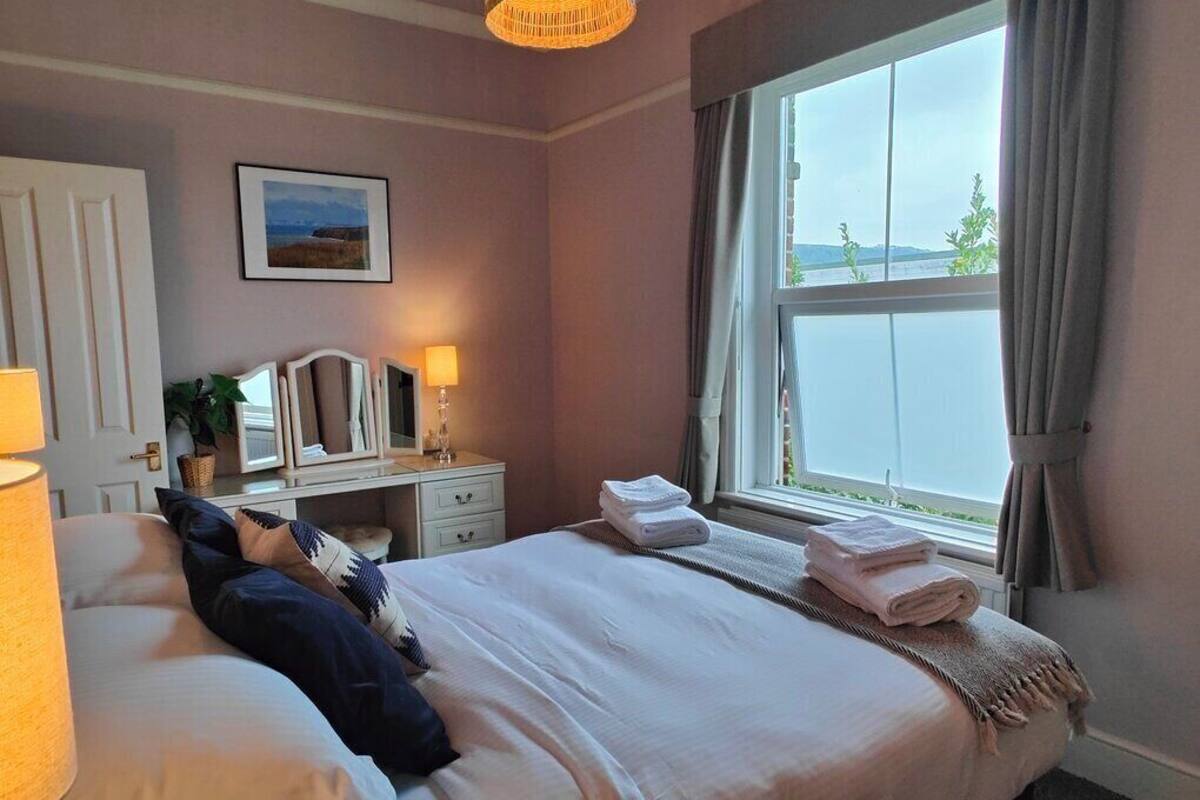 Camera d'albergo con un letto, lampade sui comodini, una scrivania con uno specchio, una finestra con tende e un quadro appeso al muro.