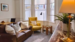 Un salon avec un canapé en cuir marron, un fauteuil jaune, une table basse en verre et un lampadaire.