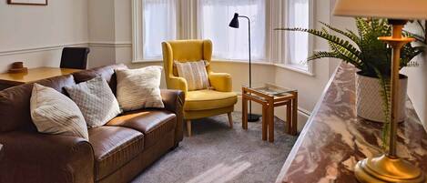 Un salon avec un canapé en cuir marron, un fauteuil jaune, une table basse en verre et un lampadaire.
