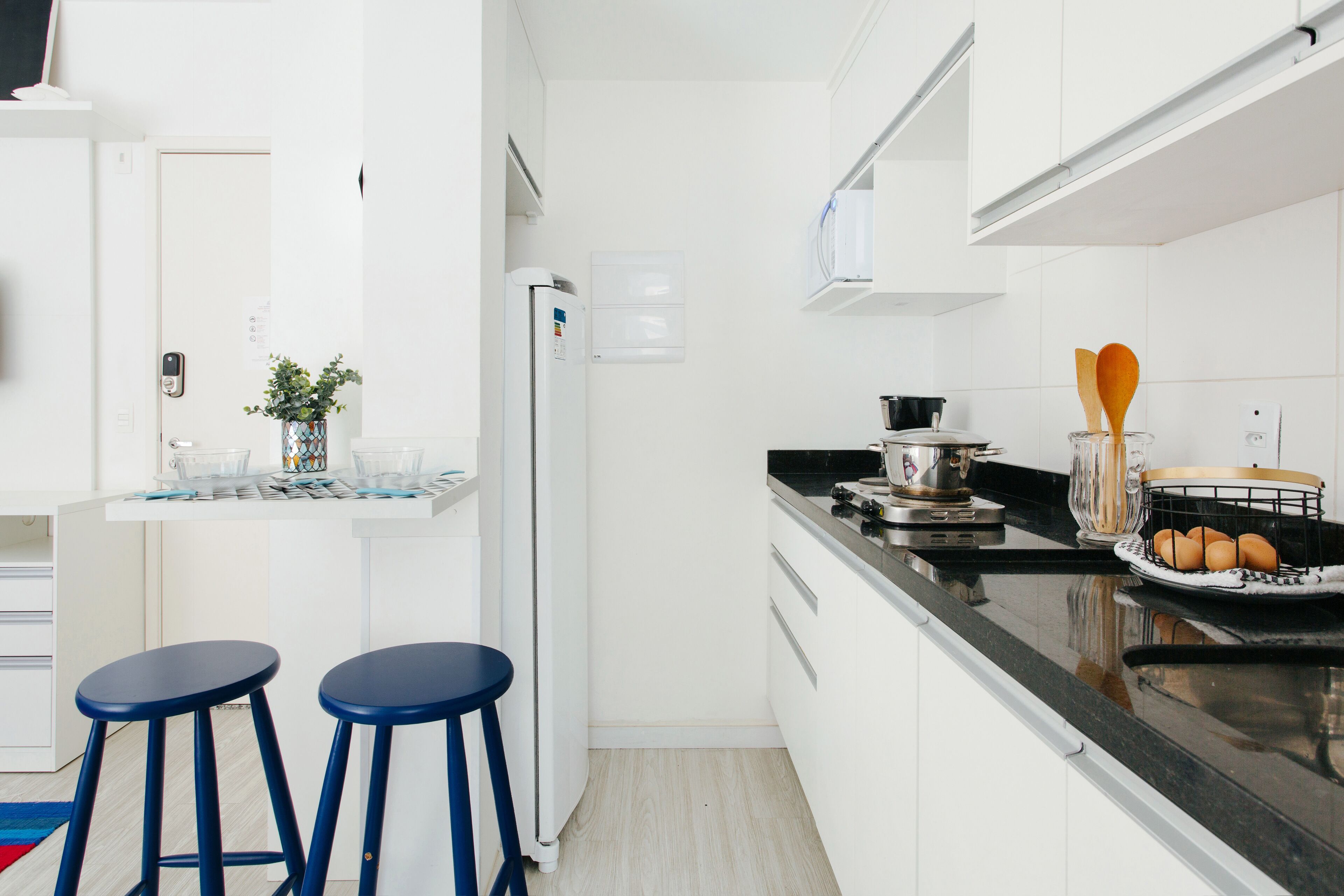A modern kitchen with white cabinets, a black countertop, and two blue stools.