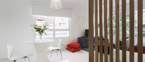 A modern living room with a glass table, white chairs, a red cushion, and a TV on a wooden cabinet.