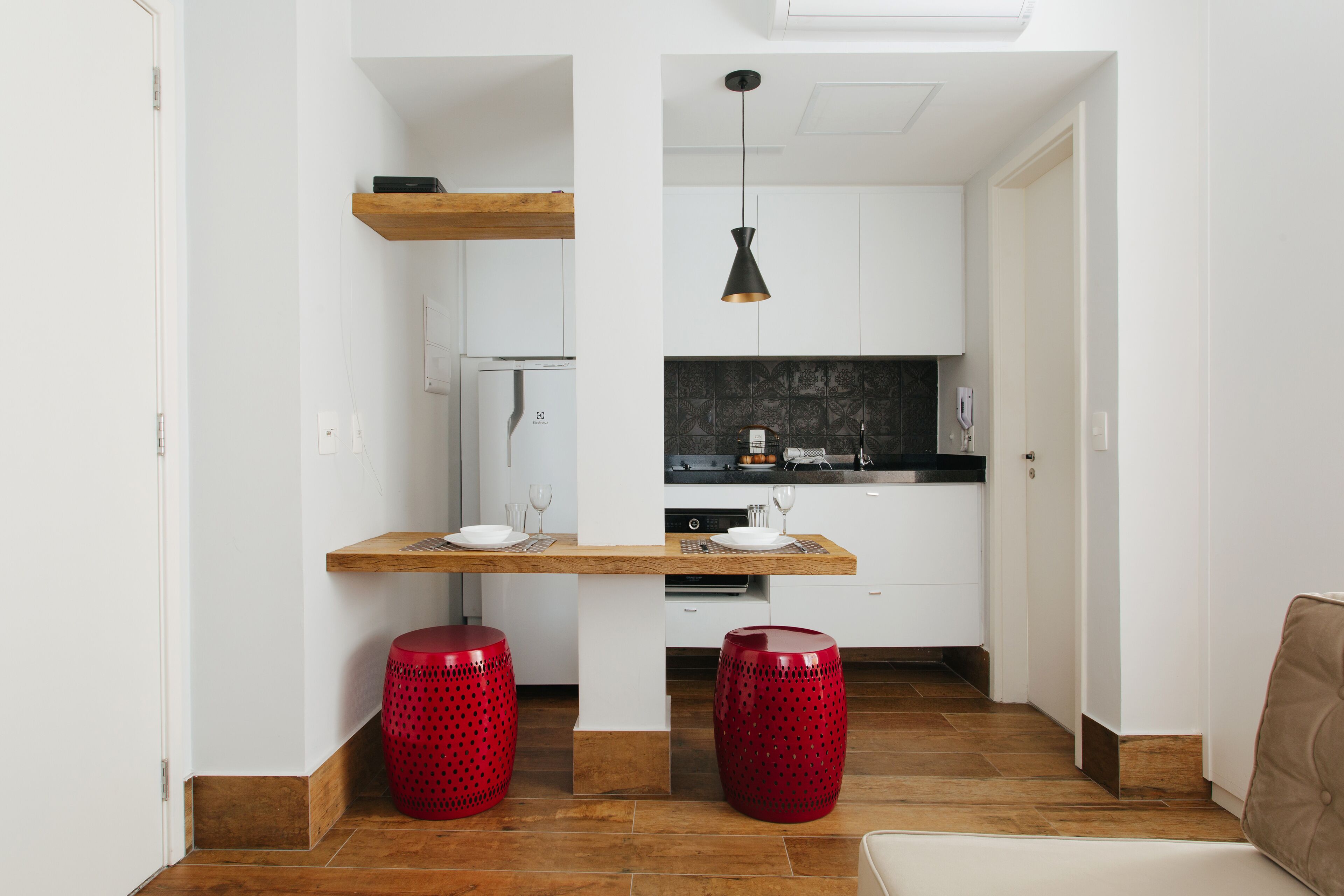 A compact kitchen with a wooden countertop, two red stools, and a hanging pendant light.