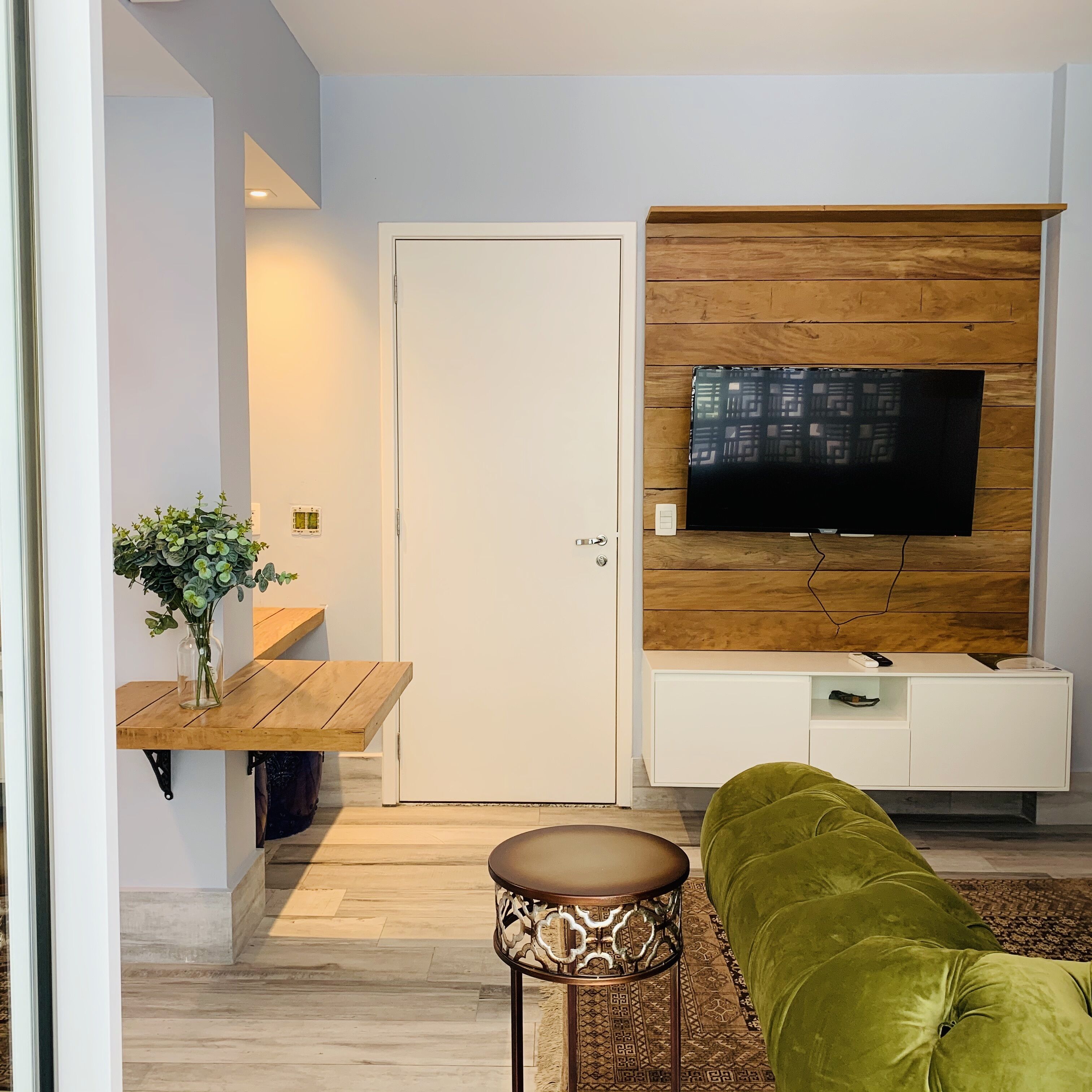 Un salon moderne avec un meuble TV en bois, un canapé vert et une petite table d’appoint.