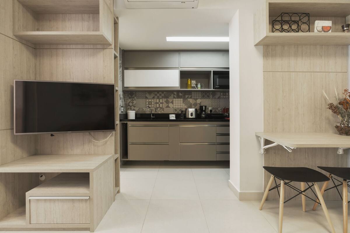 Une cuisine moderne avec des meubles en bois, un téléviseur encastré et un coin repas comprenant une petite table et des chaises.