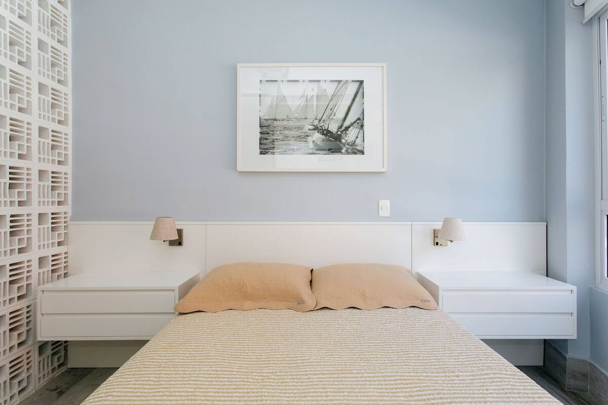 Une chambre à coucher comprenant un lit, une tête de lit, un tableau accroché au mur et une table de chevet avec une lampe.