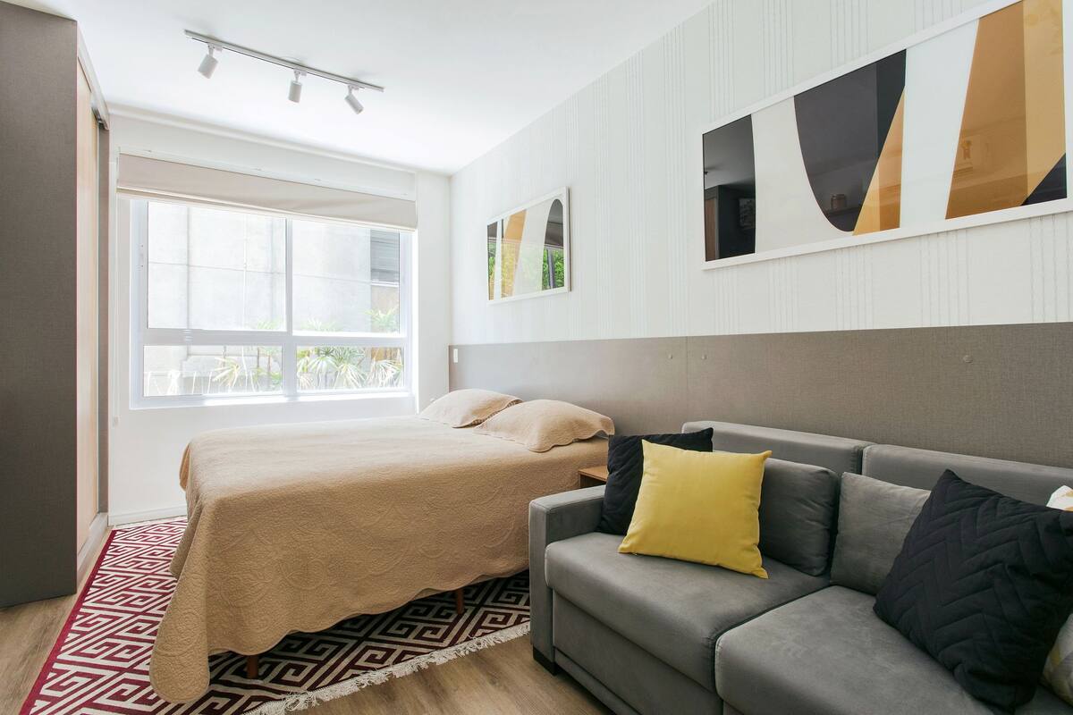 Une chambre à coucher moderne avec un lit, un canapé gris et une grande fenêtre.