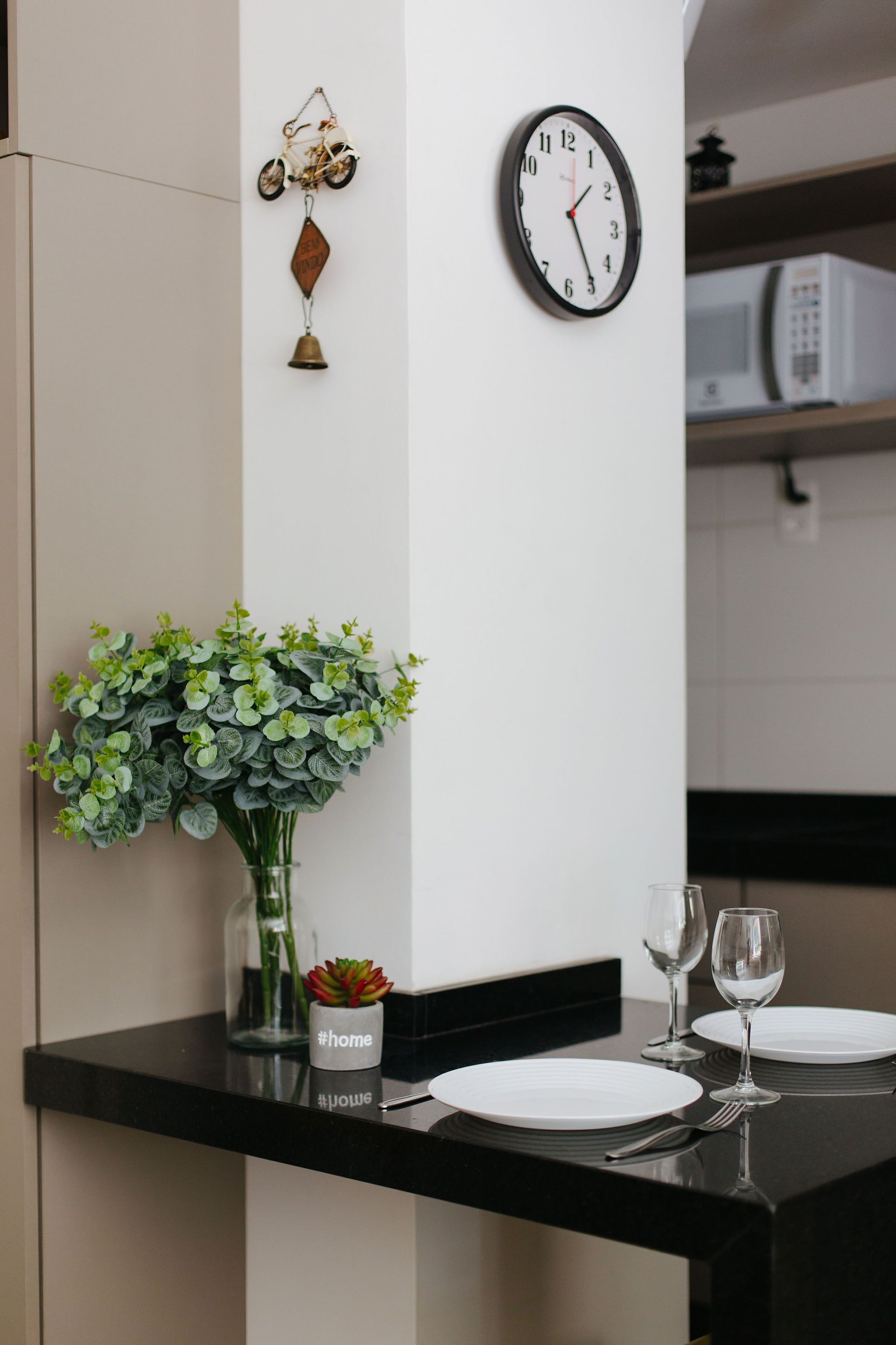 A dining area with a black countertop, white plates, and a glass vase with green foliage.