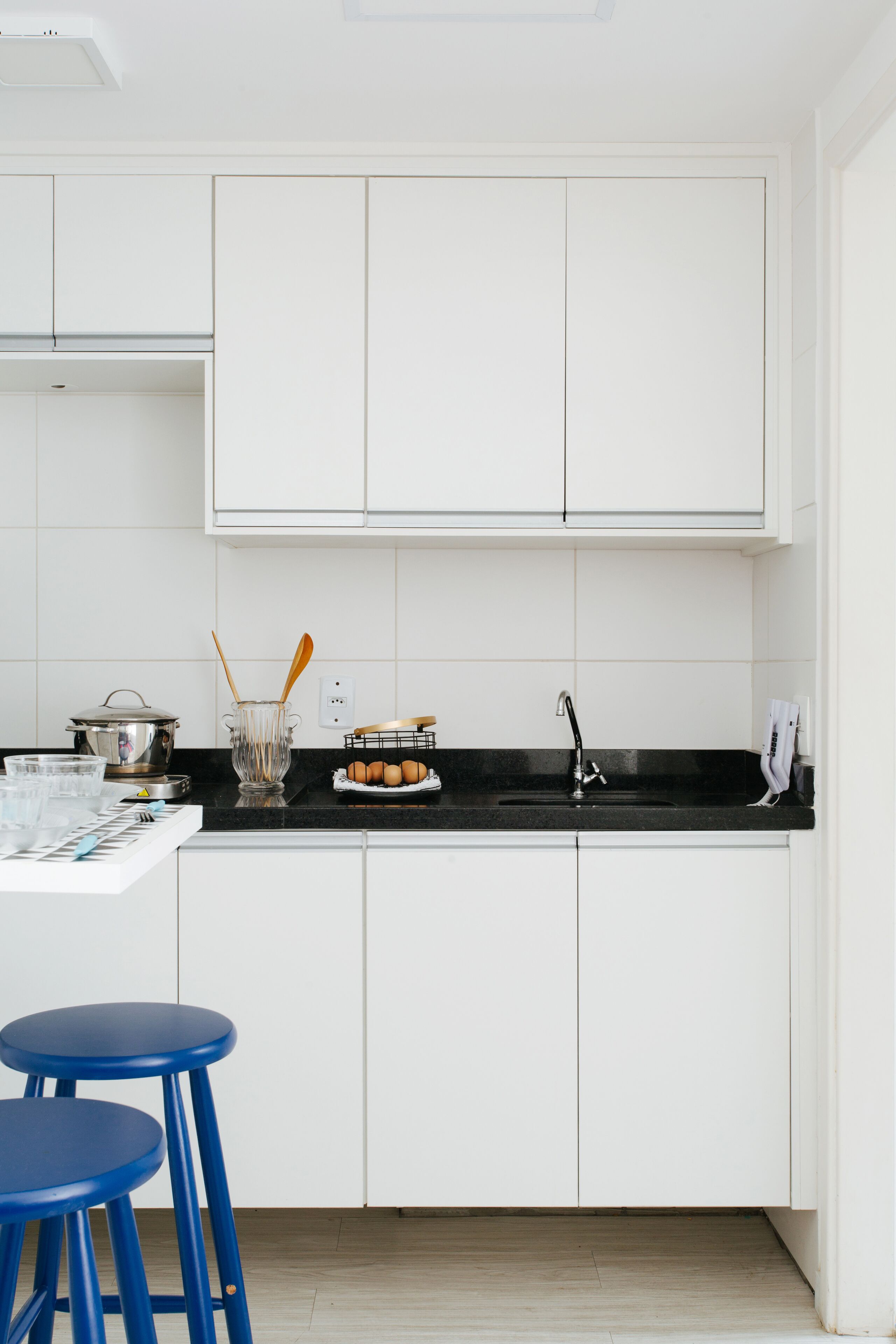 A kitchen with white cabinets, a black countertop, and two blue stools.