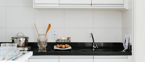 A kitchen with white cabinets, a black countertop, and two blue stools.