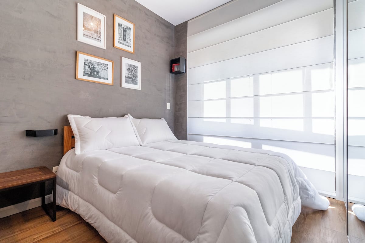 Une chambre moderne avec un grand lit, une table de chevet en bois et une fenêtre avec des stores.
