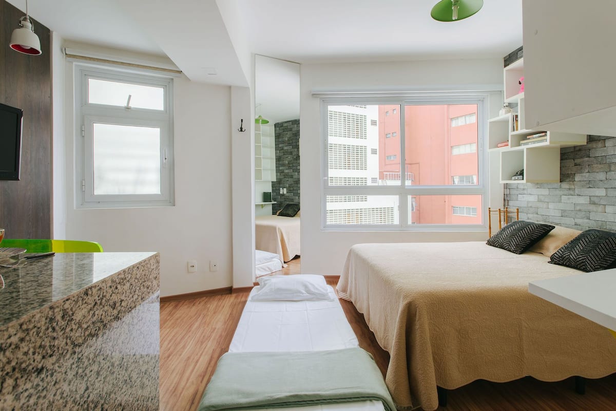 Une chambre à coucher moderne et bien éclairée, dotée d’une grande fenêtre, d’un lit, d’une table de chevet et d’une banquette intégrée.