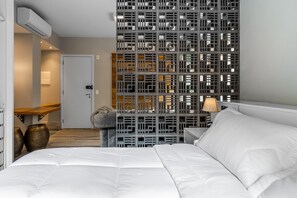 Una habitación de hotel con una cama, una mesita de noche con lámpara, un banco de madera y un panel decorativo en la pared.
