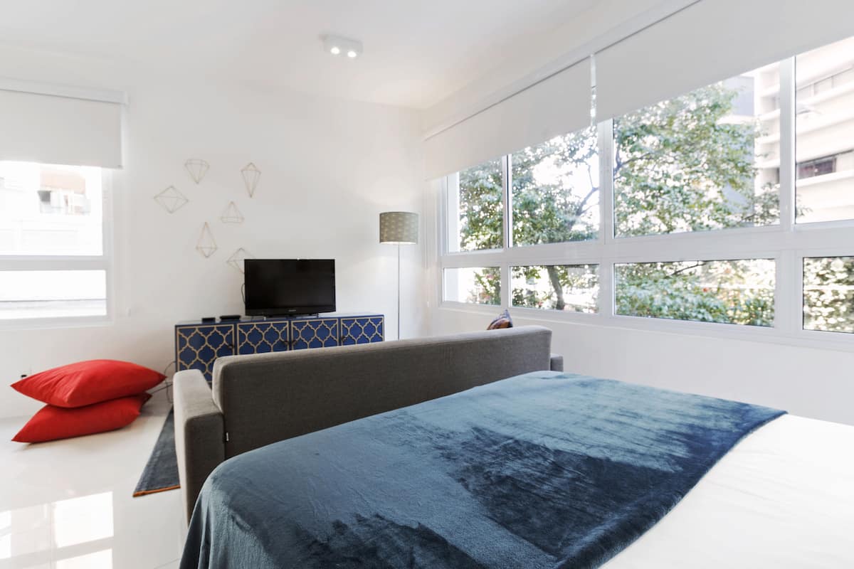 Une chambre moderne avec un grand lit, un téléviseur posé sur un meuble et une fenêtre donnant sur des arbres.