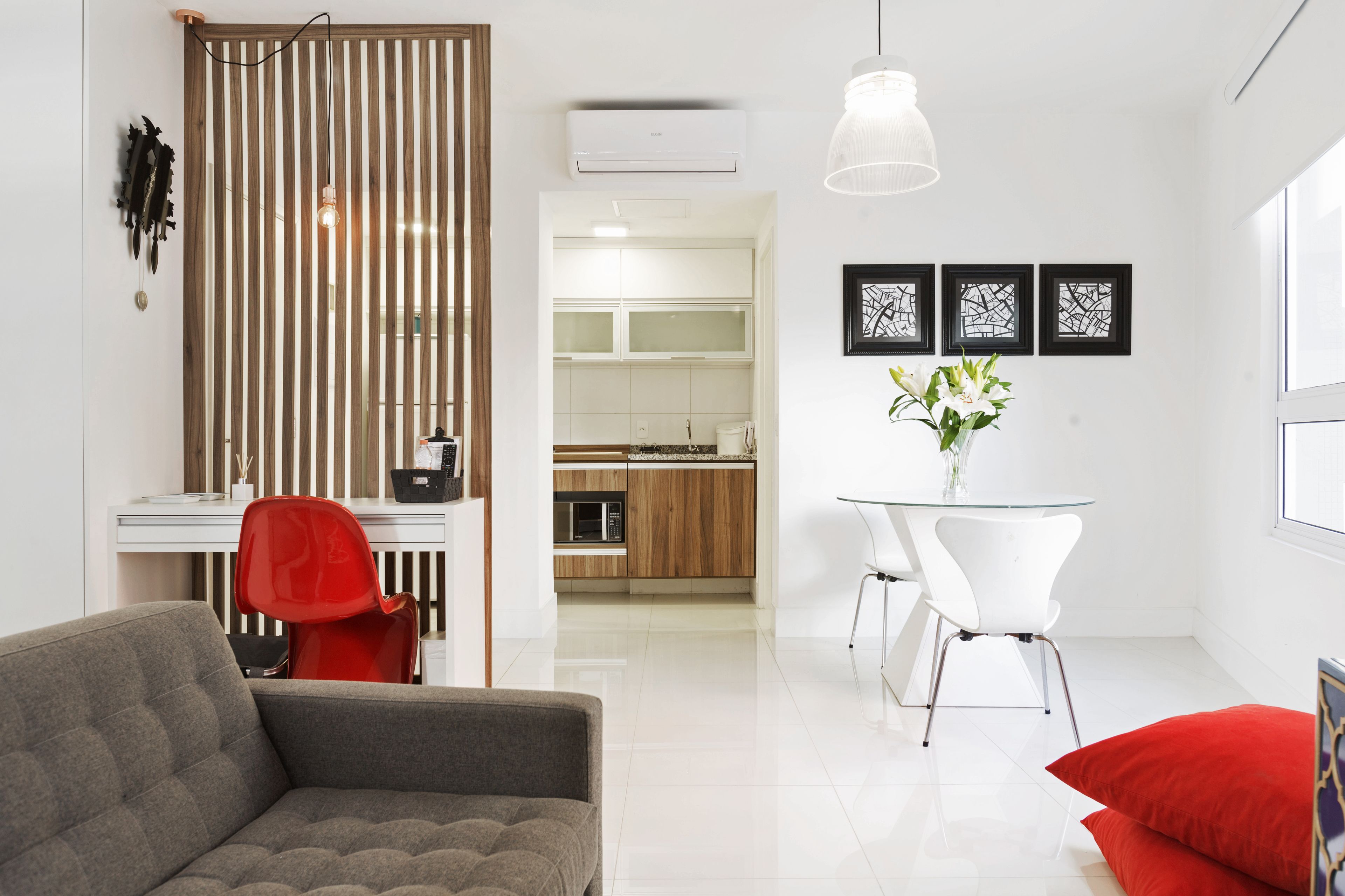 A modern living room with a sofa, a dining table with chairs, a kitchen area, and a decorative wall with framed artwork.