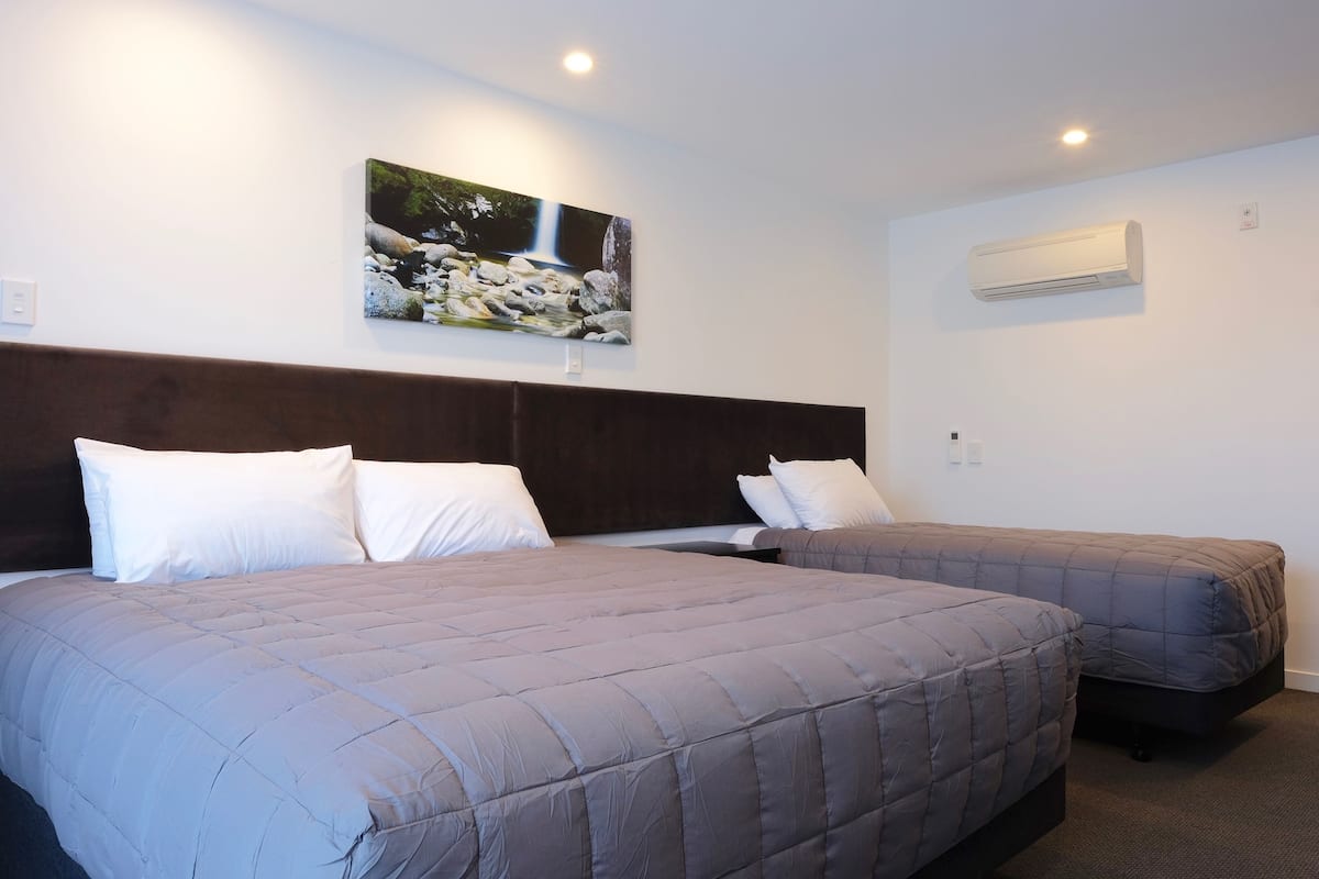 Quarto de hotel com duas camas, cabeceira, ar condicionado fixado na parede e uma pintura de uma cachoeira.