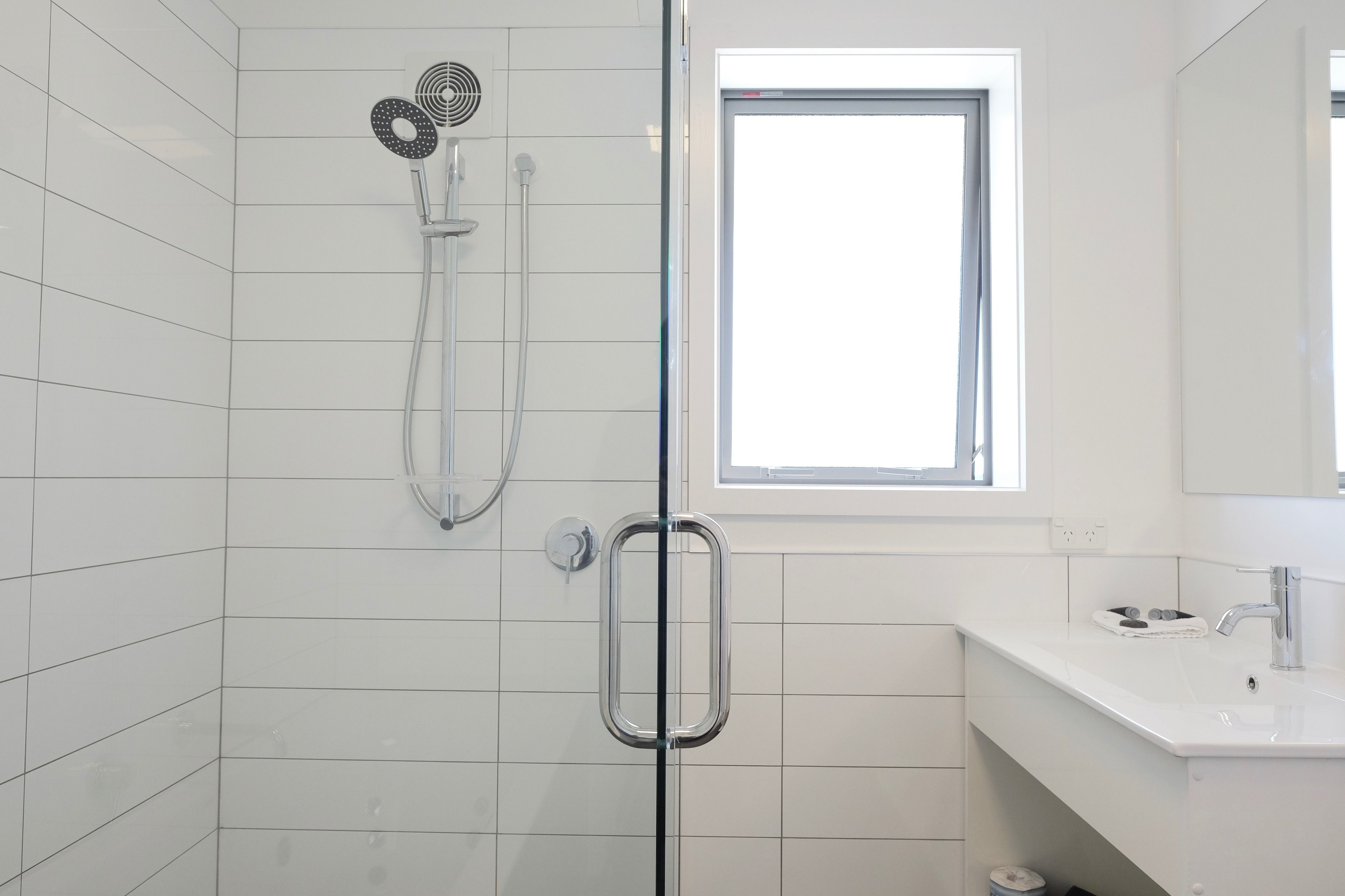 A modern bathroom with a glass shower enclosure, a white sink, and a window providing natural light.