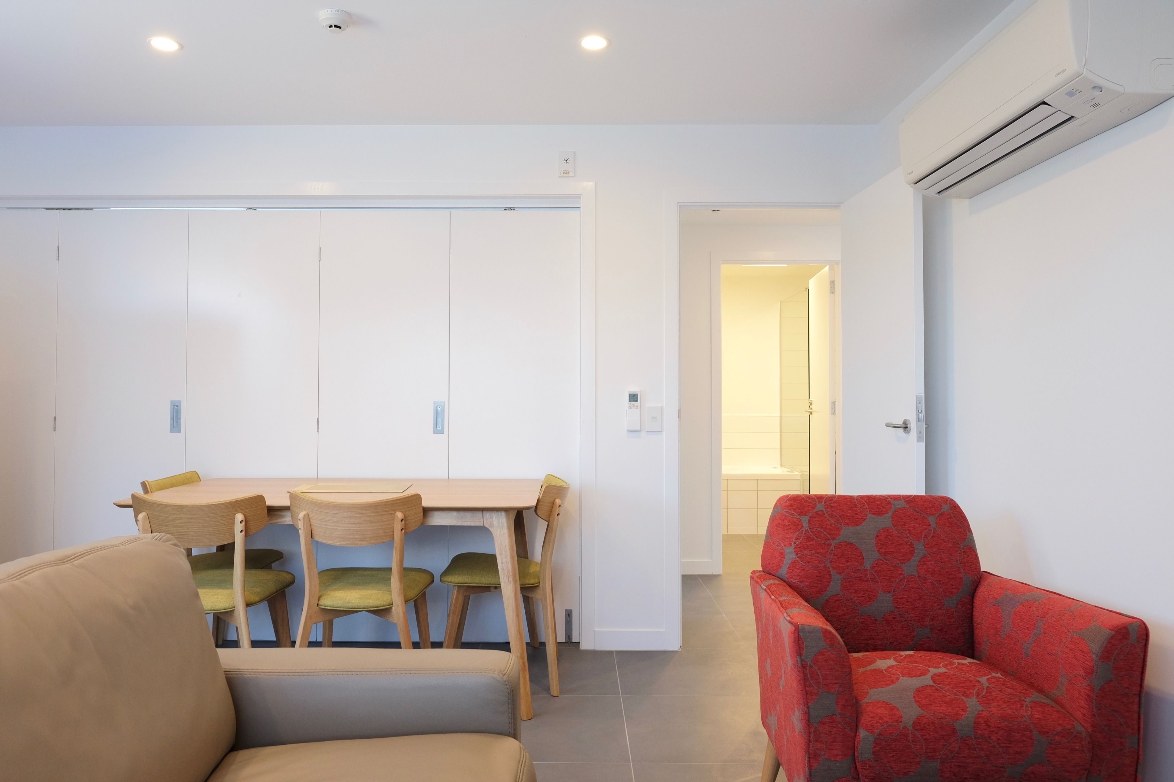 Une pièce comprenant une table à manger, des chaises, un fauteuil rouge et un appareil de climatisation.