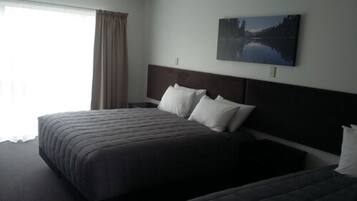 A hotel room with a large bed, a headboard, and a painting of a lake on the wall.