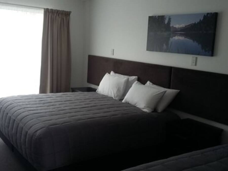 A hotel room with a large bed, a headboard, and a painting of a lake on the wall.