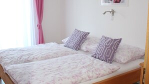 A bedroom with a wooden bed, two pillows, a wall-mounted light, and a window with curtains. - Ferienwohnung by Josef Lanzinger (Bad Vigaun)
