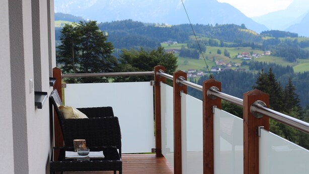 A balcony with a wooden railing, a wicker chair, and a small table with a cup and a book. - Ferienwohnung by Josef Lanzinger (Bad Vigaun)