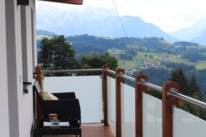 A balcony with a wooden railing, a wicker chair, and a small table with a cup and a book. - Ferienwohnung by Josef Lanzinger (Bad Vigaun)