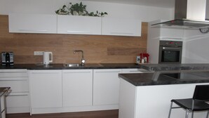 A modern kitchen with white cabinets, a stainless steel sink, a coffee maker, and a built-in oven. - Ferienwohnung by Josef Lanzinger (Bad Vigaun)