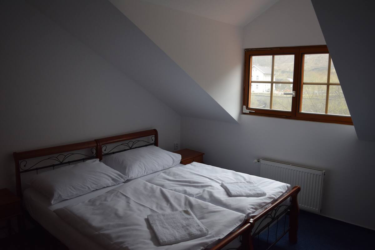 A bedroom with a wooden bed, white linens, a window, and a radiator.