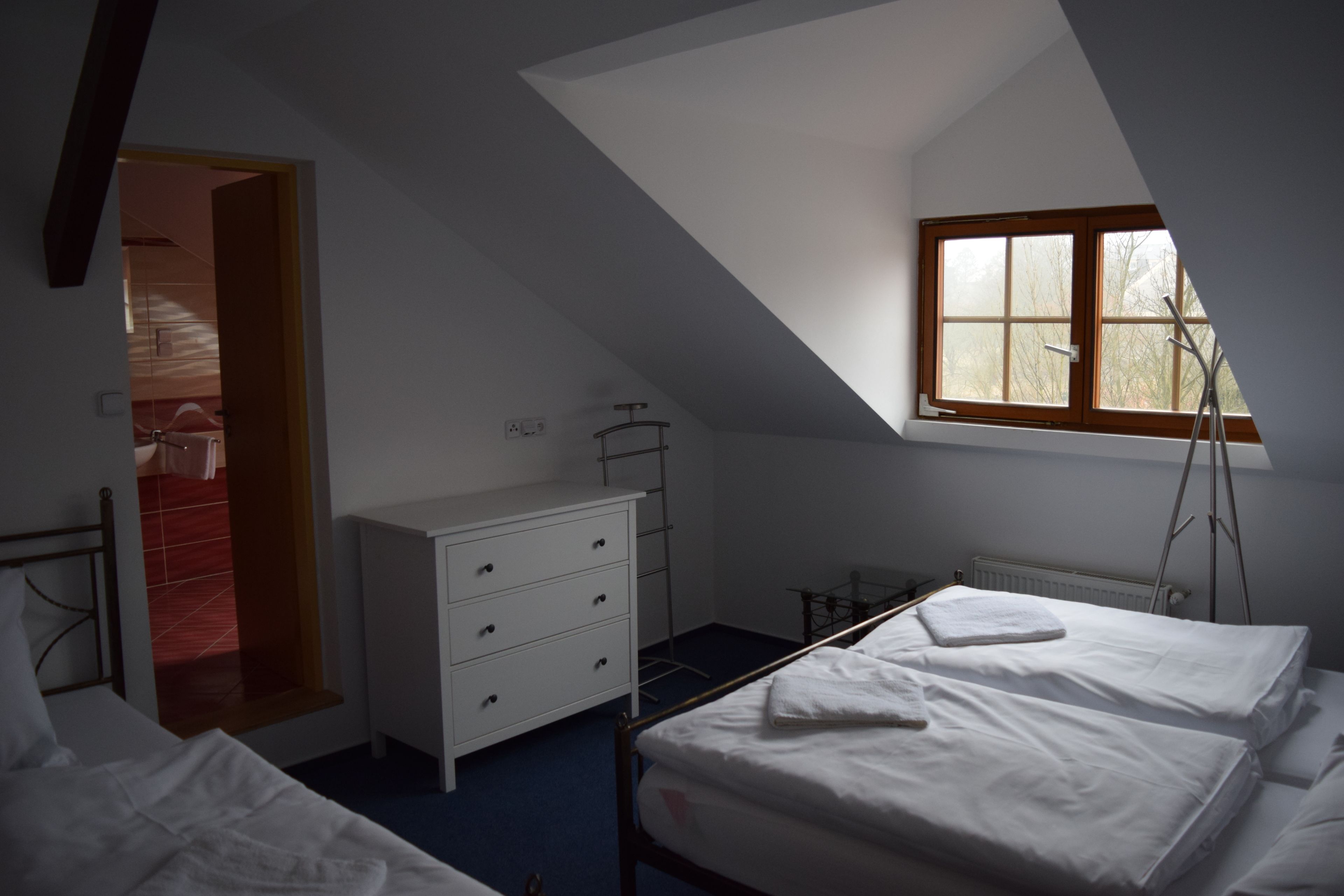 A bedroom with a sloped ceiling, a window, a bed, a dresser, and a radiator.